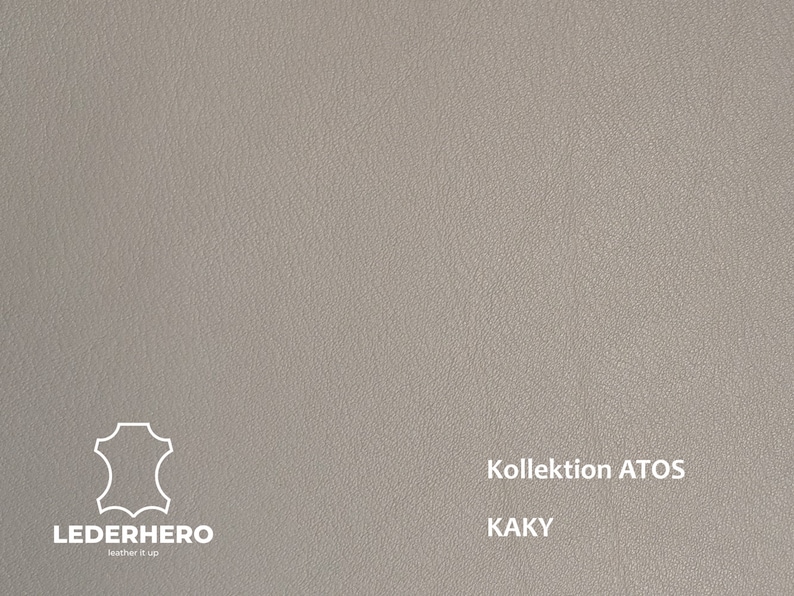 May include: A close-up of a textured, light grey leather sample. The sample is labelled "Kollektion ATOS KAKY" and features the Lederhero logo.