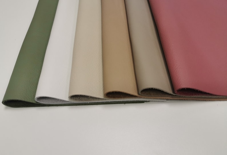 May include: A close-up of six different coloured leather swatches. The swatches are arranged in a row from left to right, with the green swatch on the left and the pink swatch on the right. The swatches are all the same size and shape.
