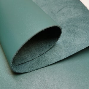 May include: A close-up of a teal leather fabric with a smooth, textured surface. The fabric is folded over, revealing a soft, suede-like underside.