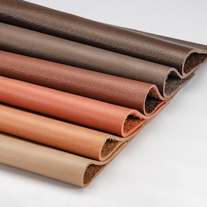 May include: Close-up of several rolled pieces of leather in varying shades of brown, from dark chocolate to tan. The edges of the leather are visible, showing the texture and color variations. The leather appears to be new and unused.