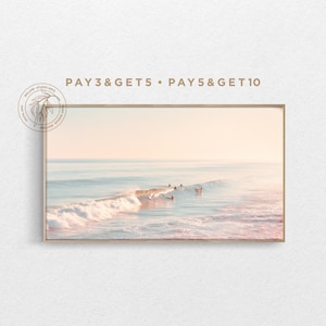 May include: A framed print of a coastal scene featuring surfers riding waves. The image has a soft, pastel color palette with shades of pink, blue, and beige. The text "PAY 3 & GET 5 • PAY 5 & GET 10" is printed at the top.