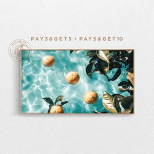 Puede incluir: Una impresión de arte mural rectangular que muestra cuatro naranjas enteras flotando en agua turquesa clara con ondas y reflejos de luz. Hojas de color verde oscuro son visibles en los bordes derecho e inferior. El texto PAY 3 & GET 5 • PAY 5 & GET 10 está impreso sobre el marco.