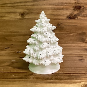 May include: A white ceramic Christmas tree with a base. The tree has a textured surface and is decorated with holes for lights.