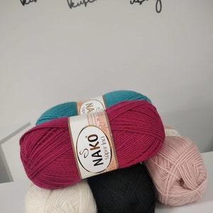 May include: Five balls of yarn in different colours: teal, burgundy, black, white, and pink. The yarn is labelled "NAKO Super İnci"