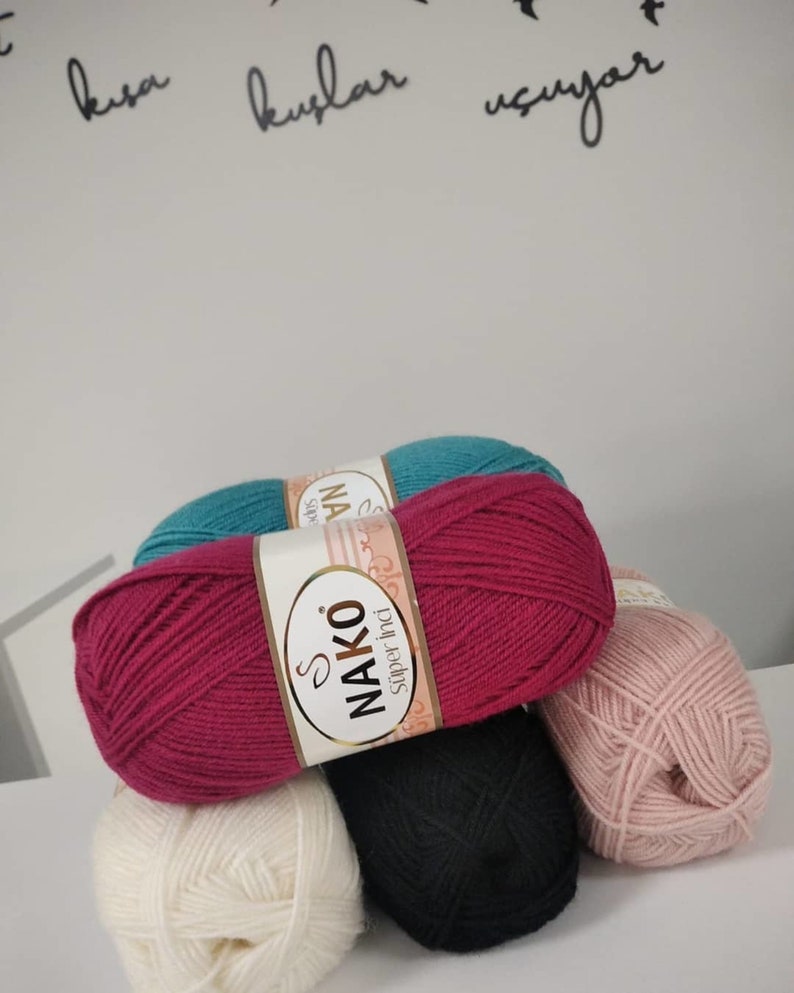 May include: Five balls of yarn in different colours: teal, burgundy, black, white, and pink. The yarn is labelled "NAKO Super İnci"