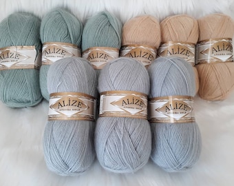 Puede incluir: Ocho ovillos de lana en tres colores: azul claro, verde claro y beige. Cada ovillo tiene una etiqueta que dice "Alize Angora Gold".