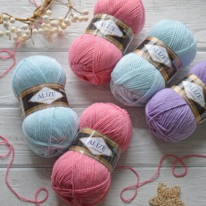 May include: Five balls of yarn in different colours: pink, light blue, purple, and a darker shade of pink. Each ball has a label that says "Alize Classic LanaGold".