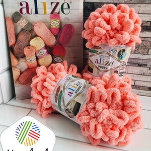 May include: A close-up of a pink ball of yarn labelled "Alize Puffy" against a white background. The yarn is soft and fluffy, ideal for crocheting or knitting.