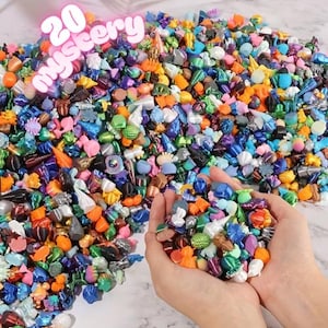 May include: A vibrant assortment of small, colorful decorative items, including various shapes and sizes. The image features a large pile of these items, with some held in cupped hands. The text "20 mystery" is displayed at the top.