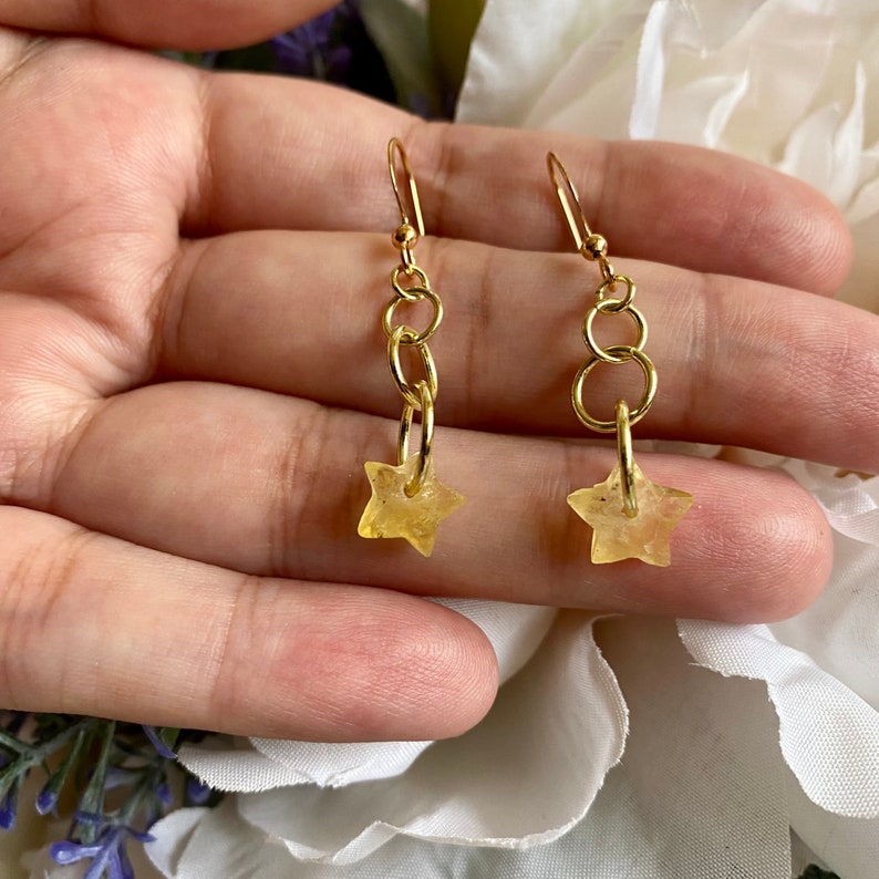 May include: Gold dangle earrings with a star-shaped charm and a chain link design.