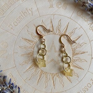 May include: A pair of gold earrings with three small gold hoops and a light yellow crystal charm on each earring.