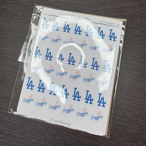 May include: A sheet of small adhesive decals featuring the blue LA Dodgers logo and the word Dodgers in blue script with a red baseball graphic. The sheet is labelled Canadian Toi and LA Dodgers - xs, with the handle @canadiantai at the bottom.