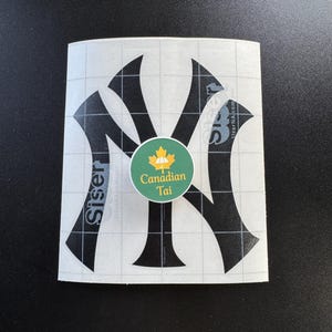 Könnte beinhalten: Ein schwarzer New York Yankees Logo-Aufkleber auf einer weißen Gitter-Transferfolie mit dem Wort Siser an der Seite. Ein runder grüner Aufkleber in der Mitte zeigt ein gelbes Ahornblatt, ein Regenschirmsymbol und den Text Canadian Tai.