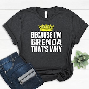 May include: A dark gray t-shirt with a yellow crown and the text "Because I'm Brenda That's Why" in white.