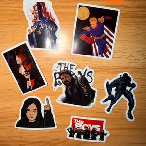 K&ouml;nnte beinhalten: Eine Sammlung von sieben Aufklebern mit Charakteren und Logos aus der Fernsehserie "The Boys". Die Aufkleber zeigen verschiedene Charaktere in Actionposen und Gruppenaufnahmen, mit leuchtenden Farben und detaillierten Kunstwerken.