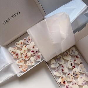 May include: Two open white boxes filled with heart-shaped wax melts. The melts are white with embedded dried flower petals in shades of red, pink, and purple. The boxes are lined with white tissue paper. The text "LINES STUDIO" is printed on the box.