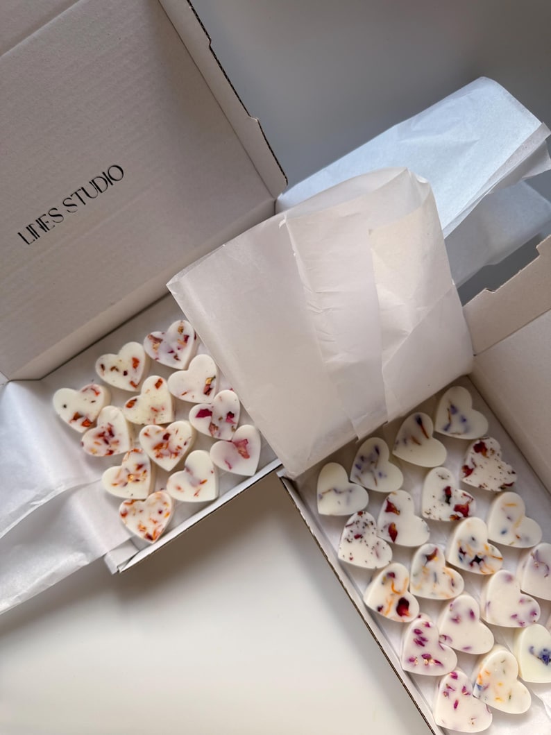 May include: Two open white boxes filled with heart-shaped wax melts. The melts are white with embedded dried flower petals in shades of red, pink, and purple. The boxes are lined with white tissue paper. The text "LINES STUDIO" is printed on the box.