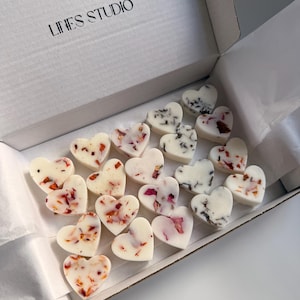 May include: A white box with the text "LINES STUDIO" contains heart-shaped wax melts. The melts are white, decorated with dried flower petals in shades of red, pink, and black. The box is open, revealing the contents.