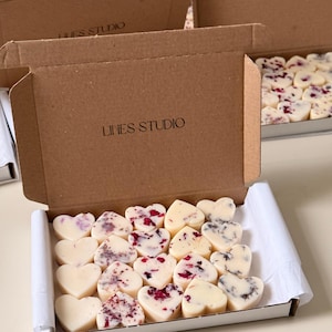 May include: Heart-shaped wax melts in a white box. Some melts are plain, while others have red and purple accents. The box is inside a larger brown cardboard box with "LINES STUDIO" printed on it.
