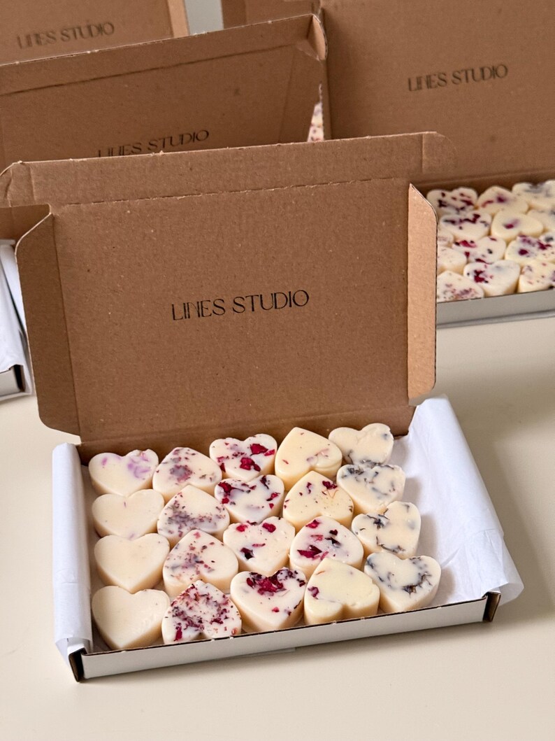 May include: Heart-shaped wax melts in a white box. Some melts are plain, while others have red and purple accents. The box is inside a larger brown cardboard box with "LINES STUDIO" printed on it.