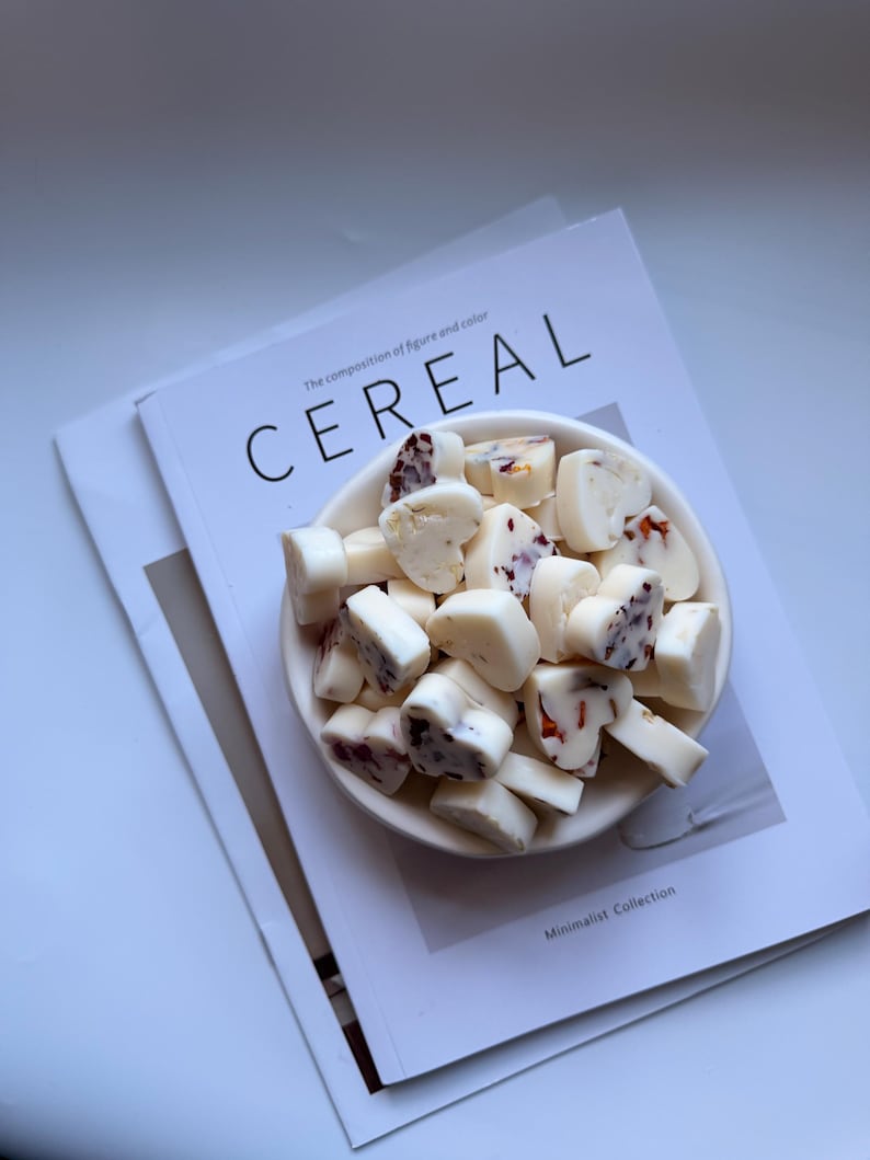 May include: A white ceramic bowl filled with heart-shaped, white-coated candies with red and brown inclusions. The bowl rests on a magazine with the word "CEREAL" in large letters. The magazine has the text "The composition of figure and color".