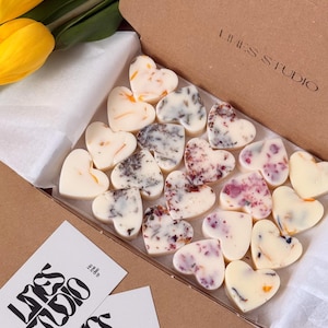May include: A box of heart-shaped wax melts with floral inclusions. The melts are white and various colors, including orange, purple, and gray. The box is brown, and the brand name "LINES STUDIO" is printed on the box and on two white cards.