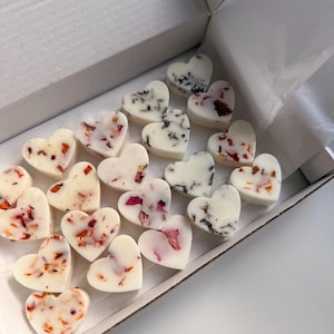 May include: A collection of heart-shaped wax melts in a white box. The melts are white and decorated with dried flower petals in shades of red, pink, and brown. The box is white and has the text "ES STUDIO" printed on the top.