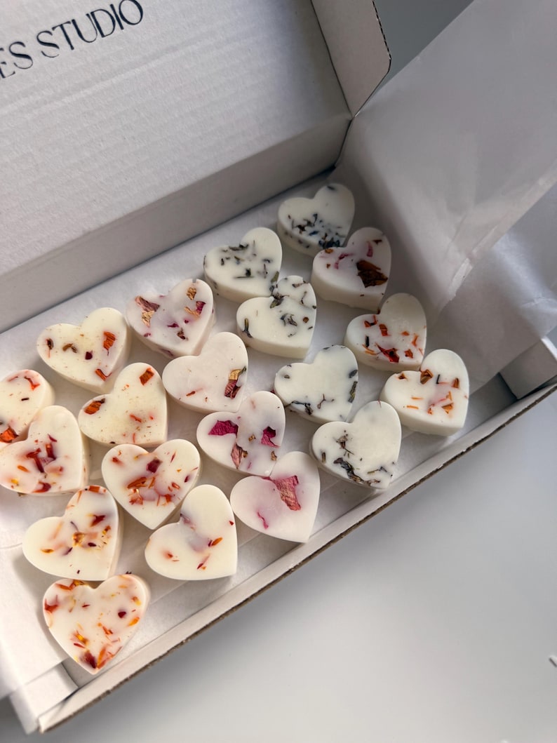 May include: A collection of heart-shaped wax melts in a white box. The melts are white and decorated with dried flower petals in shades of red, pink, and brown. The box is white and has the text "ES STUDIO" printed on the top.