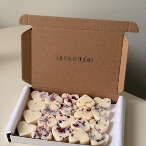 May include: A cardboard box with the text "LINES STUDIO" on the lid, open to reveal heart-shaped wax melts. Some melts are plain, while others are decorated with dried flowers. The box is lined with white paper.