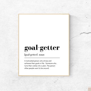 Puede incluir: Impresión enmarcada con la palabra "goal-getter" en negrita negra y su definición. La impresión tiene un fondo blanco y un marco claro. La definición describe a una persona motivada, ideal para decoración.