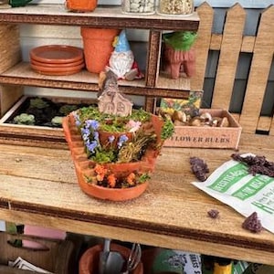 May include: A miniature wooden garden workbench with shelves, tools, and plants. The workbench has a small wooden sign that says "Flower Bulbs".