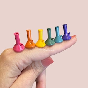 May include: A set of six miniature, conical-shaped water pipes in a rainbow gradient of pink, orange, yellow, green, blue, and purple. Each piece features a small side stem and a smooth, glossy finish. The text KayTeeKays Designs is visible.