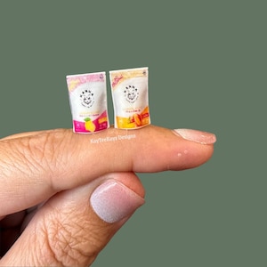 May include: Two miniature food pouches featuring the KayTeeKays Designs logo. The left pouch is white and pink with a yellow lemon graphic. The right pouch is white and orange with an apricot graphic. Both display the text KayTeeKays Designs.