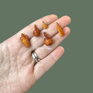 Peut inclure: Plusieurs petites bouteilles et cruches marron, dont une avec une anse, une avec un bouchon et une avec un long col. Les objets sont en matériau brun clair et sont disposés sur une main.