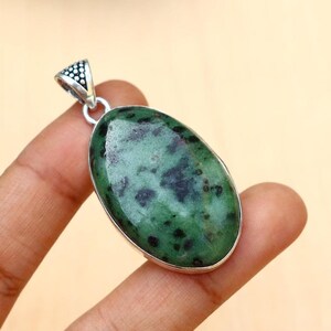 May include: A silver pendant featuring a green and black oval gemstone. The gemstone has a speckled pattern.