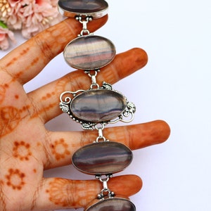 May include: A silver bracelet featuring four oval-shaped fluorite gemstones. The fluorite is a deep purple with streaks of white and grey. The bracelet is made of sterling silver and has a delicate design.