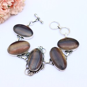 May include: A silver bracelet featuring five oval-shaped iridescent stones. The stones display a dark brown, purple, and grey colour. The bracelet has a toggle clasp.