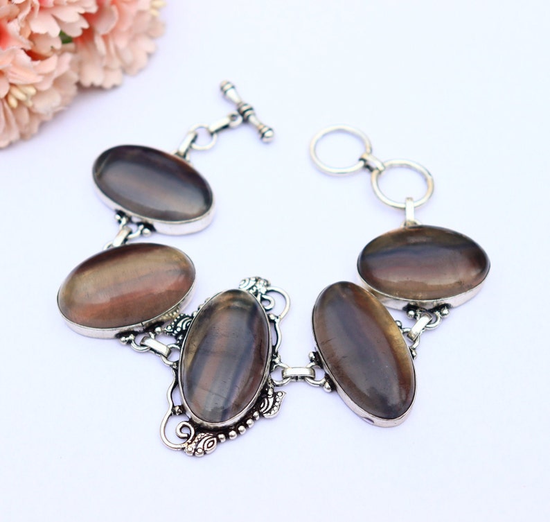 May include: A silver bracelet featuring five oval-shaped iridescent stones. The stones display a dark brown, purple, and grey colour. The bracelet has a toggle clasp.