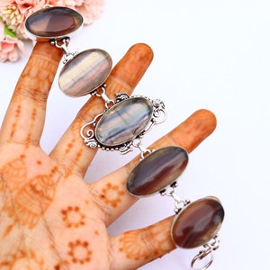 May include: A silver bracelet featuring five oval-shaped fluorite gemstones. The fluorite is a mix of purple, grey, and white.