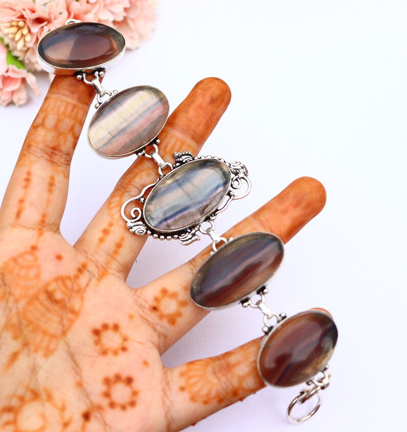 May include: A silver bracelet featuring five oval-shaped fluorite gemstones. The fluorite is a mix of purple, grey, and white.