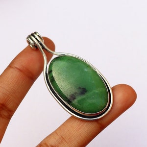 May include: A silver pendant featuring a green oval gemstone. The pendant has a simple design with a smooth, polished finish.