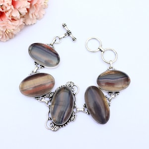 May include: A silver bracelet featuring five oval-shaped rainbow fluorite gemstones. The bracelet has a toggle clasp.