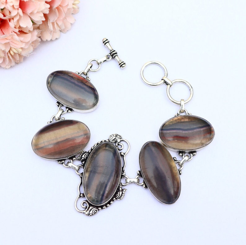 May include: A silver bracelet featuring five oval-shaped rainbow fluorite gemstones. The bracelet has a toggle clasp.