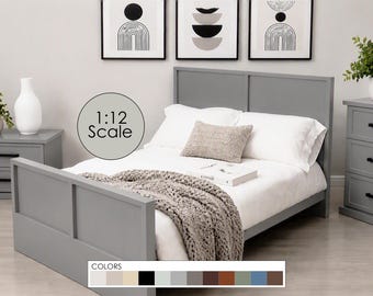 May include: A 1:12 scale miniature bed frame in a solid gray finish with a paneled headboard and footboard. The bed is dressed in white bedding, a textured gray throw blanket, and a small patterned accent pillow. A book rests on the bed.