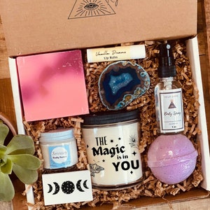 May include: A gift box filled with self-care items, including a candle that says "The Magic is in You", a bath bomb, a body spray, a bar of soap, a lip balm, and a small jar of body butter. The box is decorated with a brown paper and a small piece of agate.