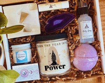 May include: A gift box filled with self-care items, including a candle with the text "Turn the Fear into Power", a body butter, a body spray, a bath bomb, a crystal, and a small white soap.