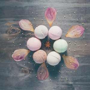 Peut inclure: Vue a&eacute;rienne de bombes de bain et de p&eacute;tales de fleurs sur une surface en bois sombre. Les bombes de bain sont de couleurs pastel vari&eacute;es, rose, blanc et vert. Les p&eacute;tales sont roses et violets. De petites perles dor&eacute;es sont dispers&eacute;es.