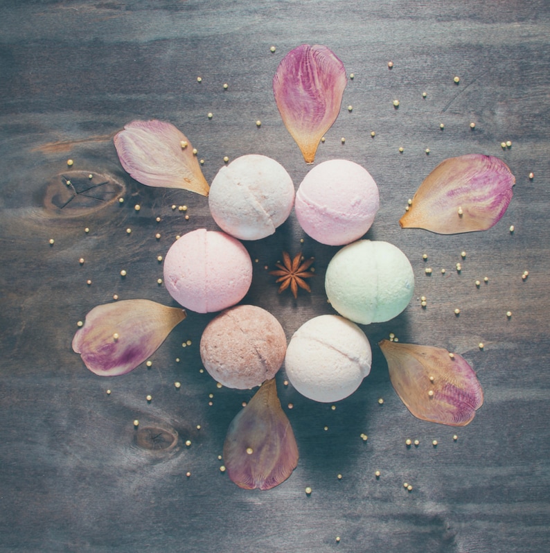 Peut inclure: Vue a&eacute;rienne de bombes de bain et de p&eacute;tales de fleurs sur une surface en bois sombre. Les bombes de bain sont de couleurs pastel vari&eacute;es, rose, blanc et vert. Les p&eacute;tales sont roses et violets. De petites perles dor&eacute;es sont dispers&eacute;es.
