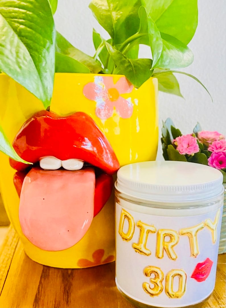 Peut inclure: Un pot de fleurs en c&eacute;ramique jaune avec un design de l&egrave;vres rouges et une langue tir&eacute;e, contenant des plantes vertes. Un pot de bougie avec le texte "DIRTY 30" en lettres dor&eacute;es et un motif de l&egrave;vres rouges est &eacute;galement pr&eacute;sent.