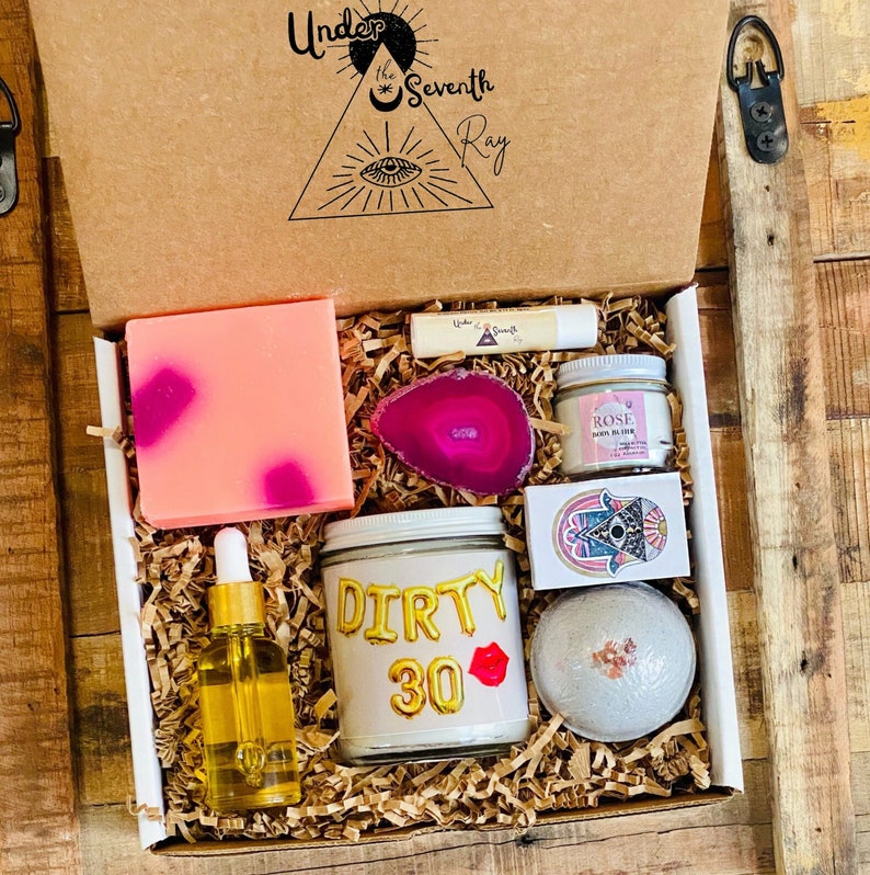 Peut inclure: Coffret cadeau rempli d'articles de bien-&ecirc;tre. Comprend un savon rose avec des taches magenta, un baume &agrave; l&egrave;vres, une tranche d'agate rose, une petite bougie, un flacon de s&eacute;rum, une bougie avec le texte "Dirty 30" et une carte d&eacute;corative.